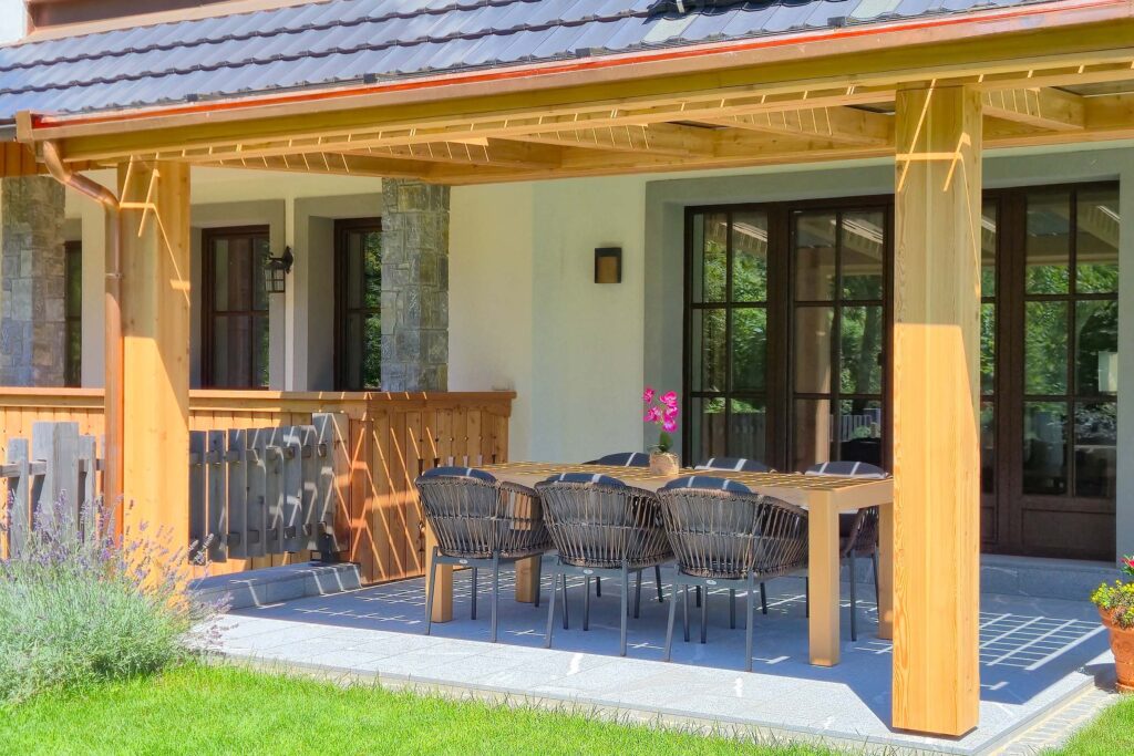 Sunny covered terrace of the luxury alpine Villa at Privillage Stare – B&B, Villa and Chalet Resort, featuring a large wooden dining table, elegant black chairs, and garden views near Lake Bohinj in Triglav National Park.